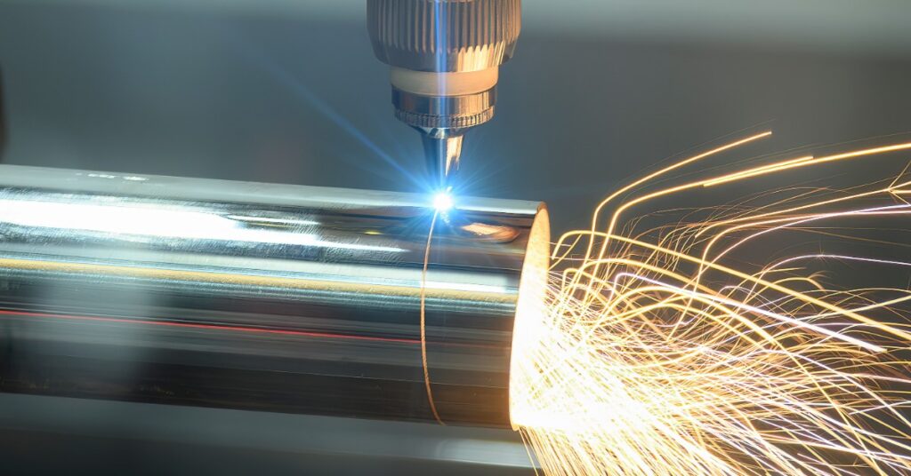 A fiber laser cutting machine cuts near the edge of a round steel tube. Bright orange sparks spray out of the tube.
