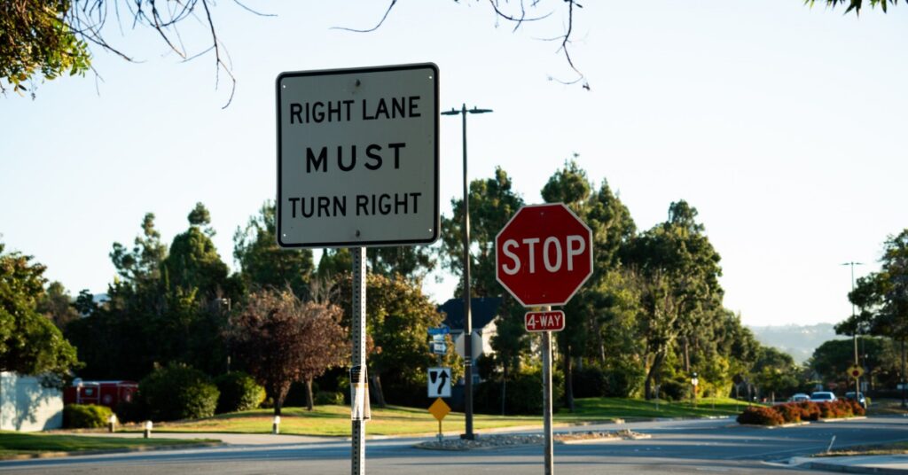 A square, white “Right Lane Must Turn Right” sign is in front of a red four-way stop sign at an intersection.